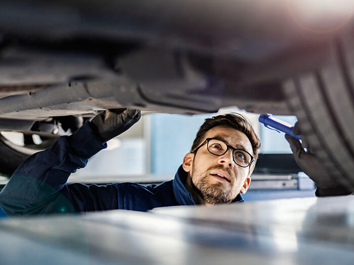 Mechanic inspecting car underside for repairs.